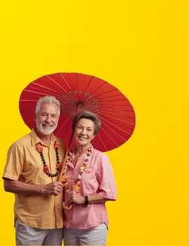 Real photo of a happy senior couple in casual summer clothes, smiling together while holding a traditional Thai umbrella (colorful Chiang Mai-style parasol) and wearing flower garlands. Warm, relaxed mood that shows they enjoy life in Thailand. Studio shot on purple gradient background, modern lifestyle photography style.